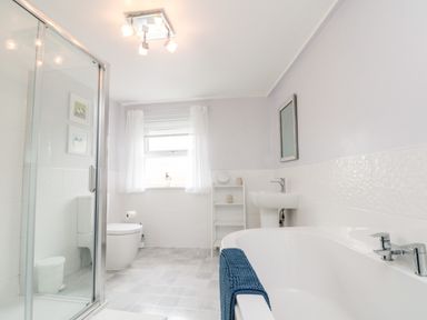 A bathroom with a bathtub a sink a toilet a shower enclosure and a window with curtains at Bluebell Cottage in Flamborough