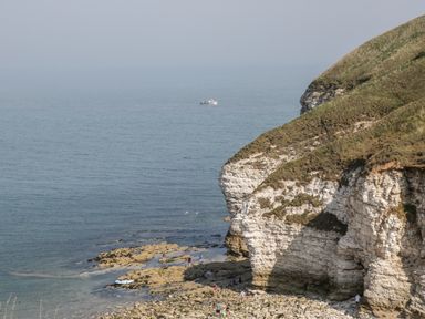 View of rocky coast with cliffs and people near the shore with a boat on the sea at Bluebell Cottage in Flamborough