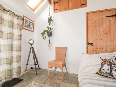 A room with a wicker chair a tripod floor lamp hanging plant plaid curtains and wooden doors at Bluebell Cottage in Flamborough