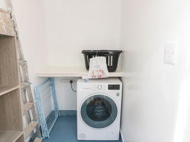 A laundry room with a washing machine a drying rack a black laundry basket and a ladder at Bluebell Cottage in Flamborough