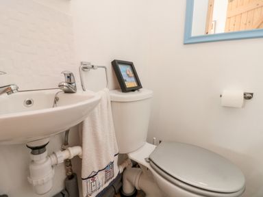 A bathroom with a sink towel toilet with a picture frame on the tank and a toilet paper holder at Bluebell Cottage in Flamborough