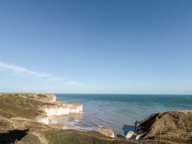 A coastal landscape with cliffs meeting the sea under a clear sky at Bluebell Cottage in Flamborough