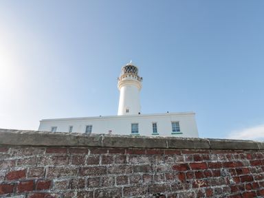 A white lighthouse behind a brick wall under a clear blue sky at Bluebell Cottage in Flamborough