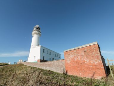 A white lighthouse and adjoining building behind a brick wall on a grassy hill at Bluebell Cottage in Flamborough