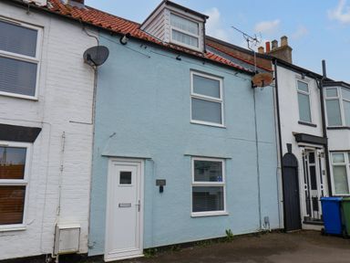 A row of terraced houses with a blue painted house in the center and white houses on either side at Bluebell Cottage in Flamborough
