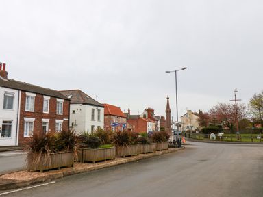 A street with brick and white houses plants in wooden planters and a monument at Bluebell Cottage in Flamborough