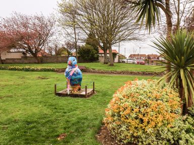 A park with a colorful bird statue on a grass field near shrubs and trees at Bluebell Cottage in Flamborough