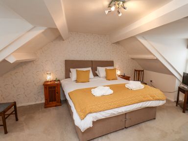 A bedroom with a large bed with yellow pillows and blanket bedside tables and chairs at Bluebell Cottage in Flamborough
