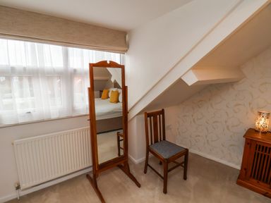 A bedroom corner with a wooden standing mirror wooden chair small wooden cabinet and a window with sheer curtains at Bluebell Cottage in Flamborough