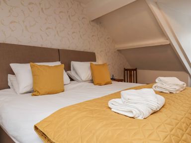 A bedroom with a double bed with yellow pillows and a yellow quilt and folded white towels on the bed at Bluebell Cottage in Flamborough