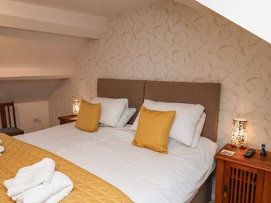 A bedroom with a double bed with yellow cushions and quilt alongside wooden bedside tables with lamps at Bluebell Cottage in Flamborough