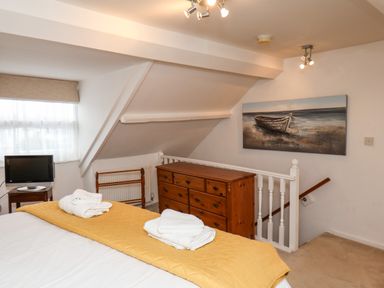 A bedroom with a bed covered by a yellow blanket and folded white towels on top a wooden dresser a small television on a side table a painting of a boat on the wall and stairs in the corner at Bluebell Cottage in Flamborough