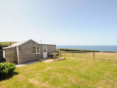 A wooden cabin with a small deck and outdoor seating overlooking the ocean at Lundy View Chalet in Widemouth Bay