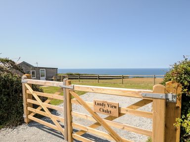 A wooden gate with a sign reading Lundy View Chalet overlooking a field and ocean in Widemouth Bay