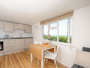 A kitchen and dining area with wooden floors and a window showing greenery and sea at Lundy View Chalet in Widemouth Bay