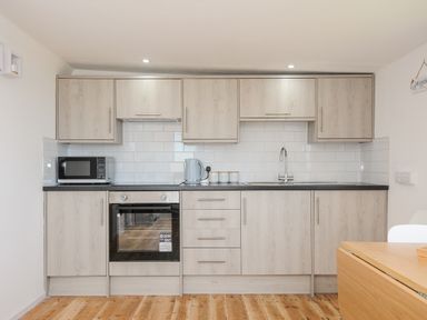 A kitchen with wooden cabinets white tiled backsplash microwave kettle oven and a wooden floor at Lundy View Chalet in Widemouth Bay