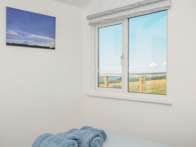 A bedroom corner with a window showing a countryside view and rolled towels on a bed at Lundy View Chalet in Widemouth Bay