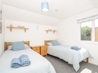 A bedroom with two single beds side by side with blue bedding and towels on the beds and wooden shelves on the walls at Lundy View Chalet in Widemouth Bay