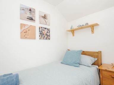 A bedroom with a wooden bed a blue pillow beach-themed wall art and a wooden shelf with decorations at Lundy View Chalet in Widemouth Bay