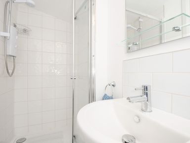 A bathroom with a shower enclosure a white sink a mirror and a blue towel at Lundy View Chalet in Widemouth Bay