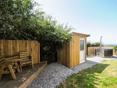 A garden area with wooden chairs on a deck a wooden shed and a hot tub at Lundy View Chalet in Widemouth Bay