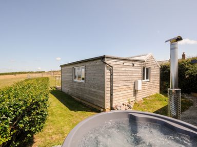 An outdoor wooden chalet with windows and a hot tub in the foreground at Lundy View Chalet in Widemouth Bay