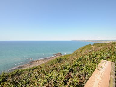 A coastal view with cliffs shrubs and a wooden bench at Lundy View Chalet in Widemouth Bay