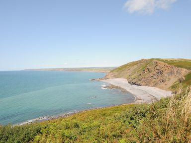 A coastal landscape with a rocky cliff and a beach beside the sea at Lundy View Chalet in Widemouth Bay