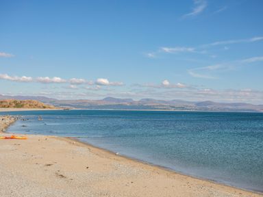 A sandy beach with calm blue water and distant hills under a blue sky at Moondunes - Pwllheli in Chwilog