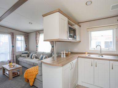A kitchen with white cabinets and a living room with a grey sofa and coffee table at Moondunes - Pwllheli in Chwilog