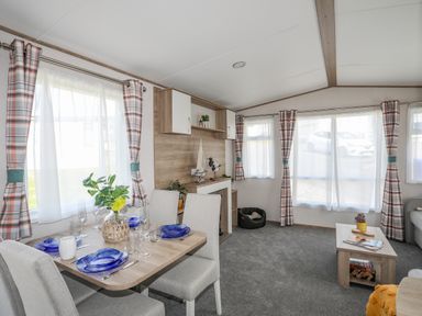 A dining area with a set table and a seating area with windows and curtains at Moondunes - Pwllheli in Chwilog