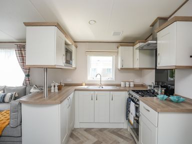 A kitchen with white cabinets a window above the sink and a stove with pots and two turquoise bowls at Moondunes - Pwllheli in Chwilog