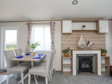 A dining area with a table set with blue plates and glasses next to a wall with a fireplace and decorative sailboat at Moondunes - Pwllheli in Chwilog