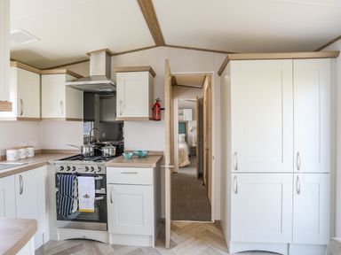 A kitchen with white cabinets a stove with two pots and towels and a fire extinguisher on the wall at Moondunes - Pwllheli in Chwilog