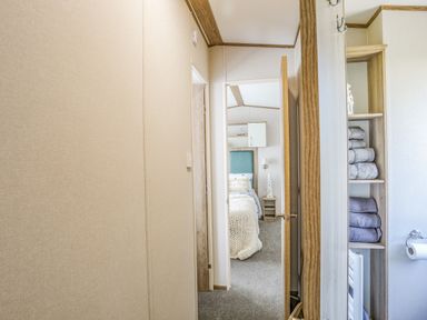 A hallway leading to a bedroom with a bed and shelves with folded towels at Moondunes - Pwllheli in Chwilog