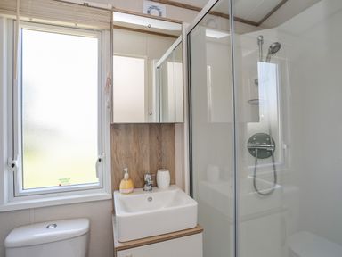 A bathroom with a shower enclosure sink with soap dispenser and cup toilet and frosted window at Moondunes - Pwllheli in Chwilog
