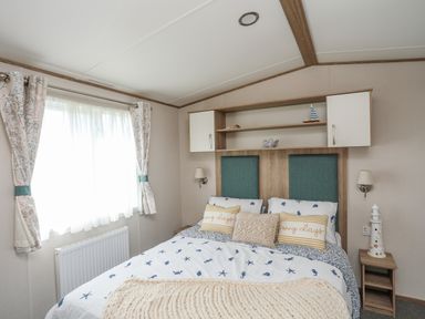 A bedroom with a bed with blue and white bedding and pillows under a shelf with cabinets and decorative items at Moondunes - Pwllheli in Chwilog