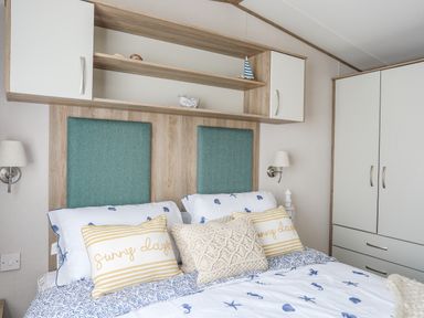A bedroom with a bed with pillows and cushions a wooden headboard with shelves and cupboards and a wardrobe at Moondunes - Pwllheli in Chwilog