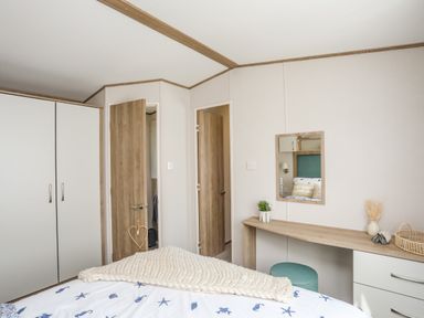 A bedroom with a bed blanket decor a wooden wardrobe a desk with a mirror and a small stool at Moondunes - Pwllheli in Chwilog