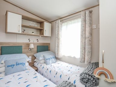 A bedroom with two single beds with fish patterned bedding and striped pillows at Moondunes - Pwllheli in Chwilog