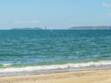 A beach with small waves and two sailboats on the sea with islands in the distance at Moondunes - Pwllheli in Chwilog