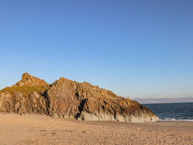 A sandy beach with large rocky outcrop near the shoreline and sea with a clear sky at Moondunes - Pwllheli in Chwilog