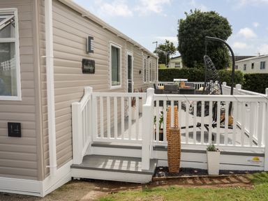 An outdoor patio area with white railing steps hanging chair and dining furniture at Moondunes - Pwllheli in Chwilog