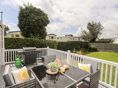 An outdoor patio with a glass table and chairs with cushions and a barbecue grill in a grassy backyard at Moondunes - Pwllheli in Chwilog