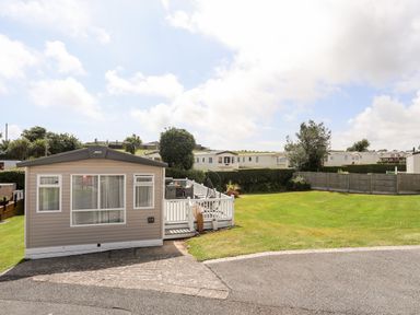 A beige static caravan with a white deck and outdoor furniture on a grassy plot with other caravans in the background at Moondunes - Pwllheli in Chwilog