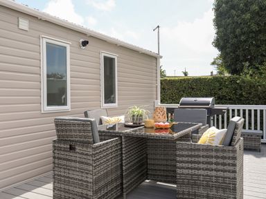 An outdoor patio with a rattan dining table and chairs a barbecue grill and plants at Moondunes - Pwllheli in Chwilog