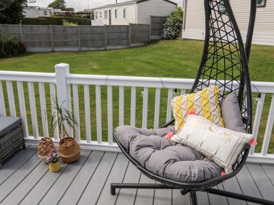 An outdoor deck with a hanging chair with cushions and potted plants on the floor at Moondunes - Pwllheli in Chwilog