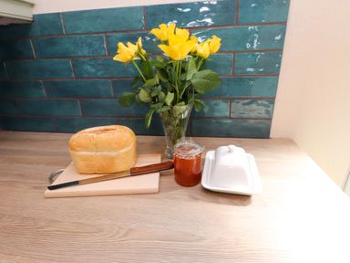 A kitchen counter with a loaf of bread on a cutting board with a knife a jar of jam a butter dish and a vase with yellow flowers at 11 Penygroes in Llanddeusant