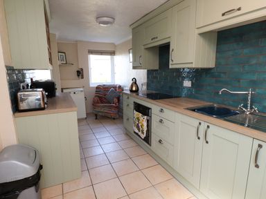 A narrow kitchen with cabinets appliances a chair and a window at 11 Penygroes in Llanddeusant