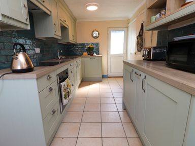 A kitchen with cabinets, a kettle, oven, toaster, microwave, and a door at 11 Penygroes in Llanddeusant